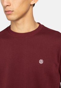 Bordeaux sweatshirt med rund hals, lavet af blød bomuld. Har et lille hvidt logo på brystet og ribbede manchetter.