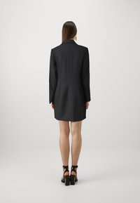 Sacou negru, croit, cu un design structurat, având guler în dublu V și mâneci lungi. Material texturat și croi slim, se termina deasupra coapselor.