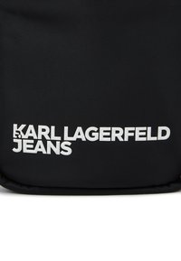 Čierna nylonová taštička s embosovaným bielym textom "KARL LAGERFELD JEANS". Hladký povrch s tvarovaním a zaoblenými hranami.