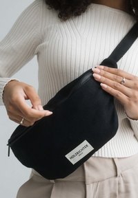 Black canvas fanny pack with a zip closure, rectangular shape, and a sewn label reading "HOLZRICHTER BERLIN." Textured fabric and adjustable strap.