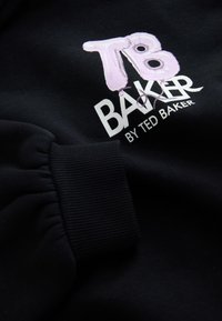 Felpa nera con polsini a costine, con logo "TB" multicolore e scritta "BAKER" stampata in bianco. Texture morbida, primo piano del dettaglio.