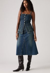 Denim komplet koji se sastoji od uskog košuljskog topa s tankim trakama i duge suknje s flared krojem, oboje u tamnoplavoj boji s svijetlim izbljeđivanjem i sirovim rubom.