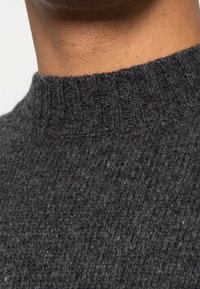 Maglione a maglia grigio scuro con colletto alto a coste. La trama appare morbida e leggermente pelosa, con un motivo sottile e irregolare.