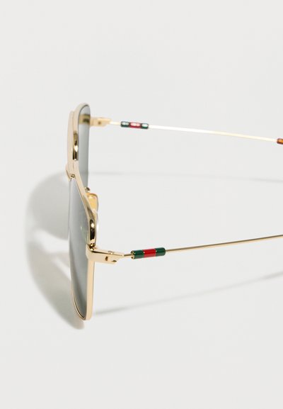 Γυαλιά ηλίου με χρυστό μεταλλικό πλαίσιο, σκοτεινούς φακούς και λεπτούς βραχίονες με πράσινες και κόκκινες σμάλτο λεπτομέρειες.