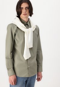 Light green button-up shirt with long sleeves, paired with a white knit scarf draped around the neck; blue denim jeans.
