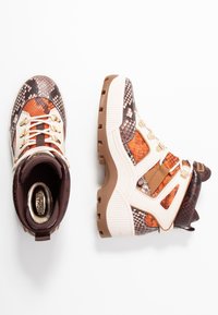 Grube sneakers na platformie w brązowym, pomarańczowym i kremowym wzorze w węża, przedstawione z widoków z góry i z boku na białym tle.