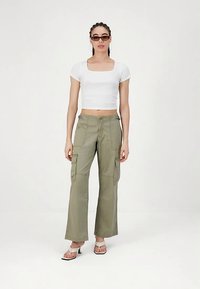 Oliivinvihreät cargo-housut, joissa on leveät lahkeet ja useita taskuja. Yhdistetty istuvaan valkoiseen lyhytpaitaan ja muhkeisiin valkoisiin sandaaleihin.