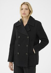 Abrigo de lana negro de doble botonadura con grandes botones, solapas anchas, bolsillos laterales y una textura suave, diseñado con un corte relajado.
