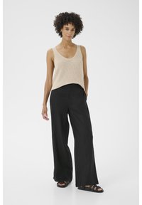 Beige gebreide tanktop gecombineerd met losse zwarte broeken, met wijde pijpen en sandalen met meerdere banden. Eenvoudig, casual outfitontwerp.