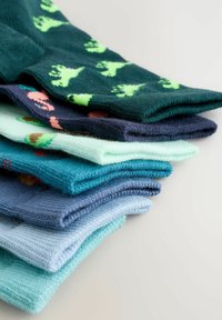 Värviliste, mustritega sokkide virn roheliste, siniste ja tumesiniste toonides, korrapäraselt asetatud heledale pinnale.