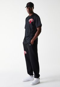 Schwarzes Baseballtrikot mit rotem "Chicago"-Schriftzug und Logo, kombiniert mit schwarzen Sweatpants im ähnlichen Design und weißen Sneakers.