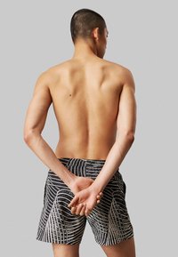 Costume da bagno a righe bianche e nere con vita elastica, caratterizzati da design a linee ondulate e vestibilità comoda, con la schiena del modello visibile.