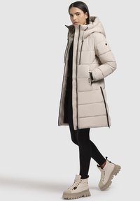 Beeg punutud jakk kapuutsi, vertikaalne õmblus, tõmblukuga taskud ja must tõmblukk. Kanda mustade retuuside ja beežide sidumiskatega saabastega.