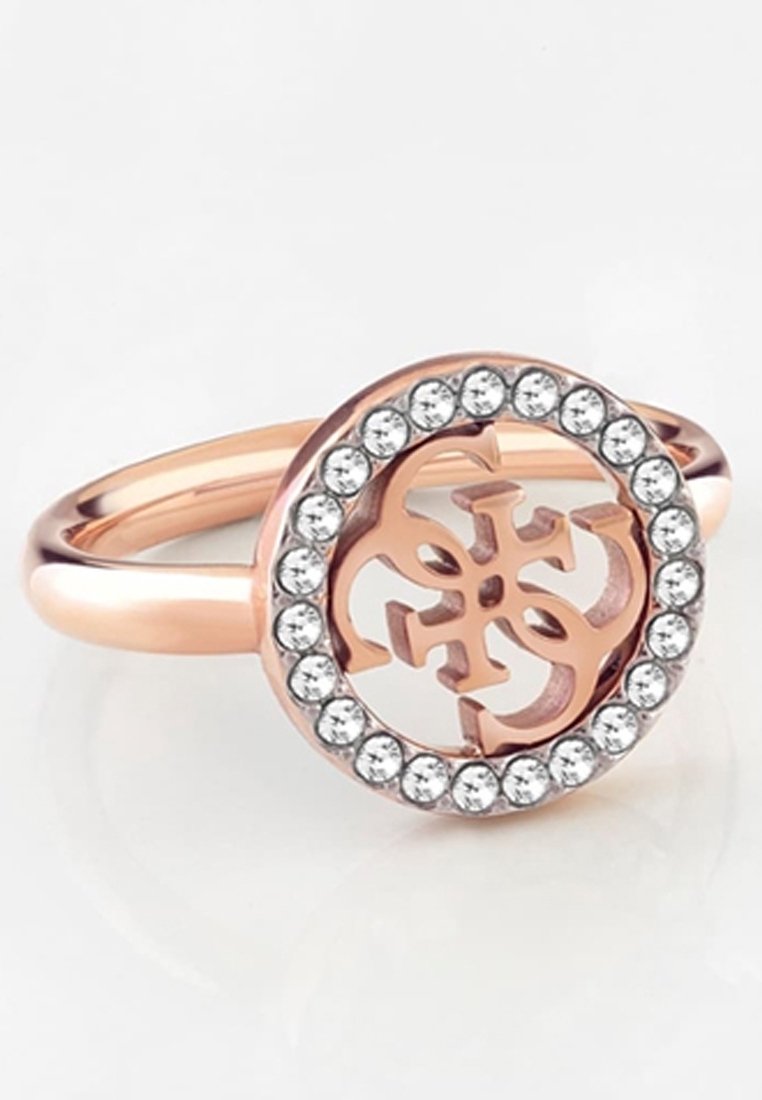 Bague en or rose avec un emblème circulaire présentant un motif complexe entouré d'une bordure de cristaux clairs et ronds.