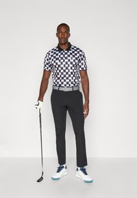 Black and white checkered polo shirt, short sleeves, with a collar. Paired with black pants and white shoes with blue accents. Golf club in hand.