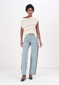 Off-white strikket topp med korte ermer, kombinert med lyseblå vide jeans med svarte sidelister, komplementert med svarte høye hæler.