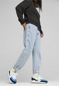Hellblaue Denim-Jeans mit lockerer Passform, kombiniert mit mehrfarbigen Sneakers, die blaue, grüne und schwarze Akzente haben. Schwarzer Sweatshirt.