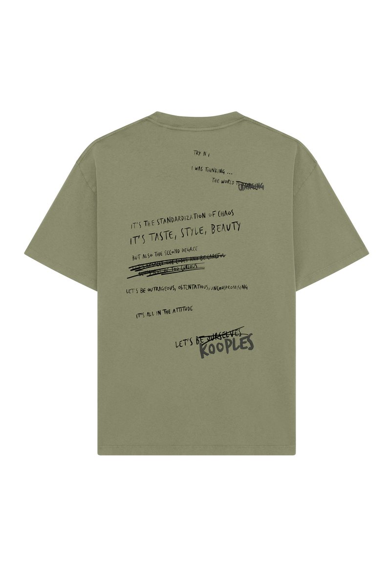 Camiseta de algodón verde oliva con mangas cortas. La parte posterior presenta varios elementos de texto impresos en negro contrastante, algunos tachados.