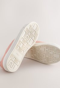 Baskets roses avec des semelles blanches à motifs montrant un dessin géométrique et le nom de la marque « NEXT » embossé en dessous.