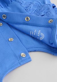 Abbigliamento per bambini di colore blu con bottoni a pressione lungo la cucitura, caratterizzato da un ricamo floreale e un'etichetta del marchio visibile all'interno.