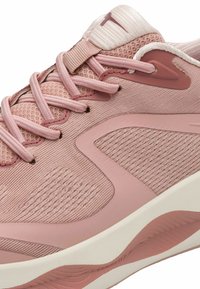 Light pink athletic shoe featuring a textured mesh upper, smooth overlays, and a cushioned sole with subtle wave patterns.