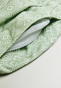 Zöld mintás szövet fehér pöttyökkel és geometriai formákkal, réteges dizájnnal és belső texturált fehér hálós béléssel.