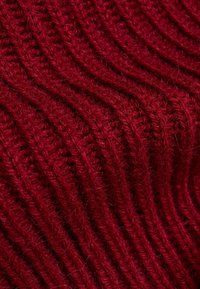 Tissu tricoté rouge avec une texture côtelée, présentant des lignes parallèles et des fibres douces et duveteuses pour une chaleur accrue.