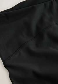 Detailný záber hladkej čiernej tkaniny s viditeľným švom prebiehajúcim diagonálne cez povrch.