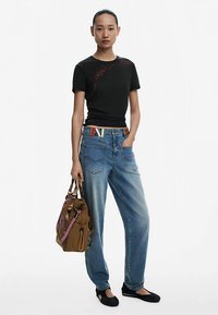 Čierne tričko s krátkym rukávom s červeným prešívaním, svetlomodré voľné rifle, hnedá taška s vzorovaným popruhom a čierne balerínky.