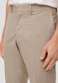Světle béžové kalhoty s přizpůsobeným střihem, plochým předním dílem, jemnou texturou a bočními kapsami. Obsahují poutka na opasek a mají slim fit design.