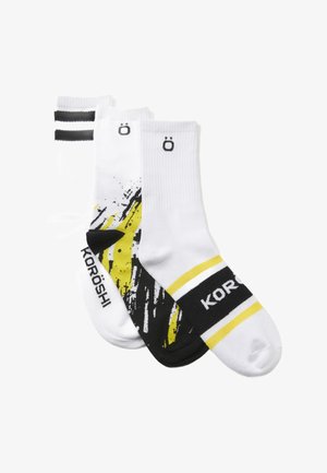 Three pairs of socks: one with black and yellow graphic print, one white with black stripes, and one solid white with logo.