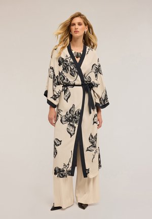 Floral-patterned, beige kimono with black accents. Features a tie belt, wide sleeves, and a deep V-neck. Worn over beige wide-leg pants.