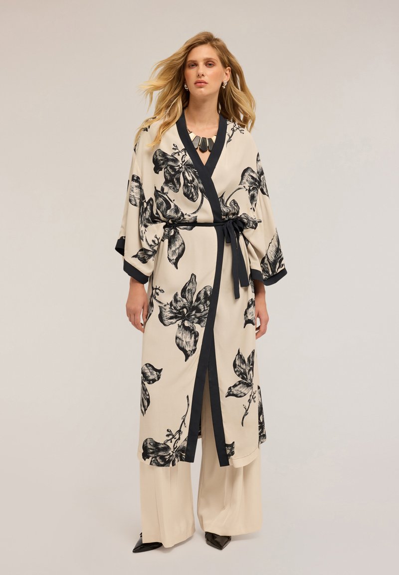 Kimono s květinovým vzorem v béžové barvě s černými akcenty. Obsahuje opasek na zavázání, široké rukávy a hluboký výstřih do V. Nosené přes béžové široké kalhoty.