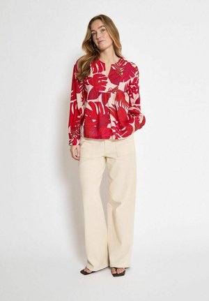 Top rosso a fiori con maniche lunghe e scollatura rotonda, abbinato a pantaloni a gamba larga color crema. Tessuto liscio, con motivi a foglia prominenti.
