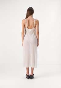 Vestido de tela ligera y transparente con un corte largo y recto. Presenta tirantes finos y un diseño de espalda baja. El color es principalmente blanco con una textura sutil.