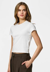 T-shirt court en coton blanc avec manches courtes, col rond et silhouette ajustée. Assorti à un pantalon taille haute marron.