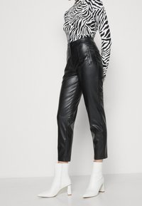 Svarta fusk läderbyxor med hög midja, sidofickor med dragkedja och tapered ben, i kombination med en svart och vit zebrastroppad topp och vita ankelstövlar.