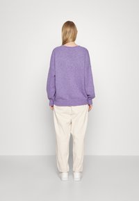 Maglione oversized in lavanda con polsini e orlo a coste, abbinato a pantaloni beige chiaro e sneaker bianche. Texture morbida.