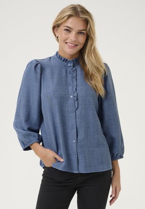 Blaue Bluse mit Knopfleiste und gerafftem Kragen, langen Puffärmeln mit elastischen Bündchen, aus einem leichten strukturierten Stoff.