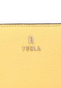 Cartera de cuero amarilla con una superficie texturizada, que presenta un logotipo plateado de "Furla". Los bordes están ribeteados en negro para crear contraste.