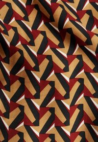 Tissu géométrique rouge, noir et or avec des formes angulaires répétées et des couleurs contrastées. Texture lisse avec un motif audacieux et moderne.