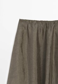 Jupe légère marron avec taille élastique froncée et texture froissée suspendue devant un fond blanc.