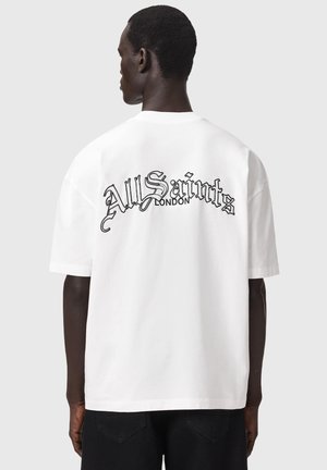 Homme de dos portant un t-shirt blanc oversize avec l'inscription "AllSaints London" en lettres gothiques noires sur la partie supérieure du dos.