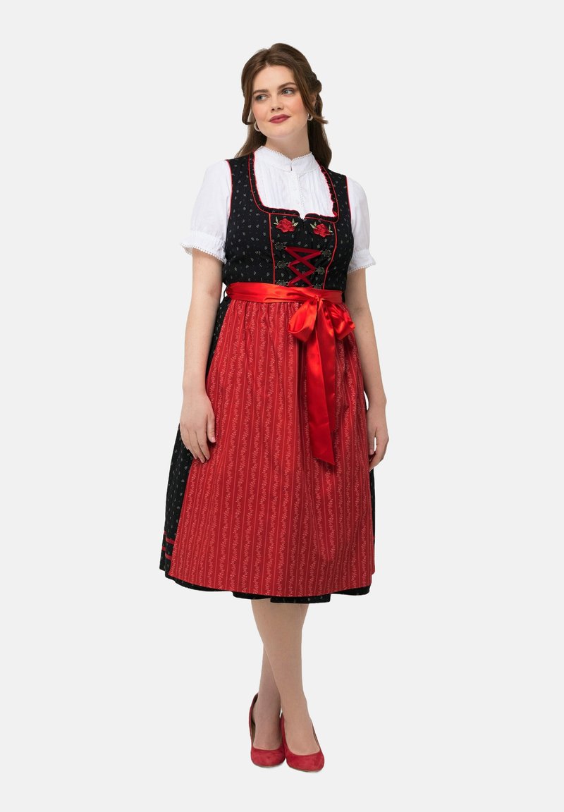 Traditionele kleding met een zwarte lijfje versierd met bloemmotieven, een rode rok met verticale strepen en een felrode satijnen riem.