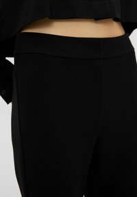 Leggings neri in un tessuto morbido ed elastico con un design aderente. Presentano una vita alta e senza cuciture visibili.