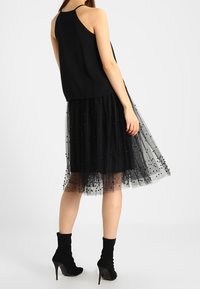 Top noir sans manches associé à une jupe en tulle noire jusqu'aux genoux, ornée de pois et à la coupe superposée. Porté avec des bottines noires.