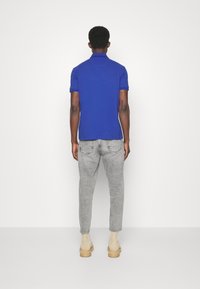 Královsky modré polo tričko s měkkou texturou, krátkými rukávy a límcem, spárované se světle šedými vypasovanými džíny a hnědými kotníkovými botami.