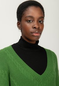 Maglione verde a maglia con scollo a V e motivi testurizzati, indossato sopra un dolcevita nero, caratterizzato da una texture liscia e un design pulito e strutturato.