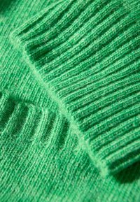 Groene gebreide stof met ribbeltextuur, die verschillende diktes en vezels toont, met een zachte uitstraling.