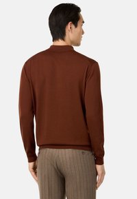 Ruda ilga rankovė polo marškinėliai su rausvais krašteliais ir rankogaliais, derinami su smėlio spalvos juostuotais kelnių. Minkšto džemperio tekstūra, tvarkingas dizainas.